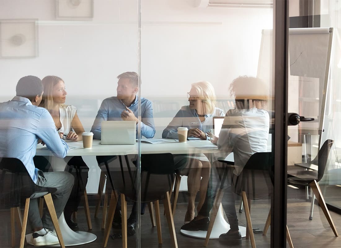Business Insurance - View Through the Glass of a Group of Employees Sitting Around a Table During a Business Meeting
