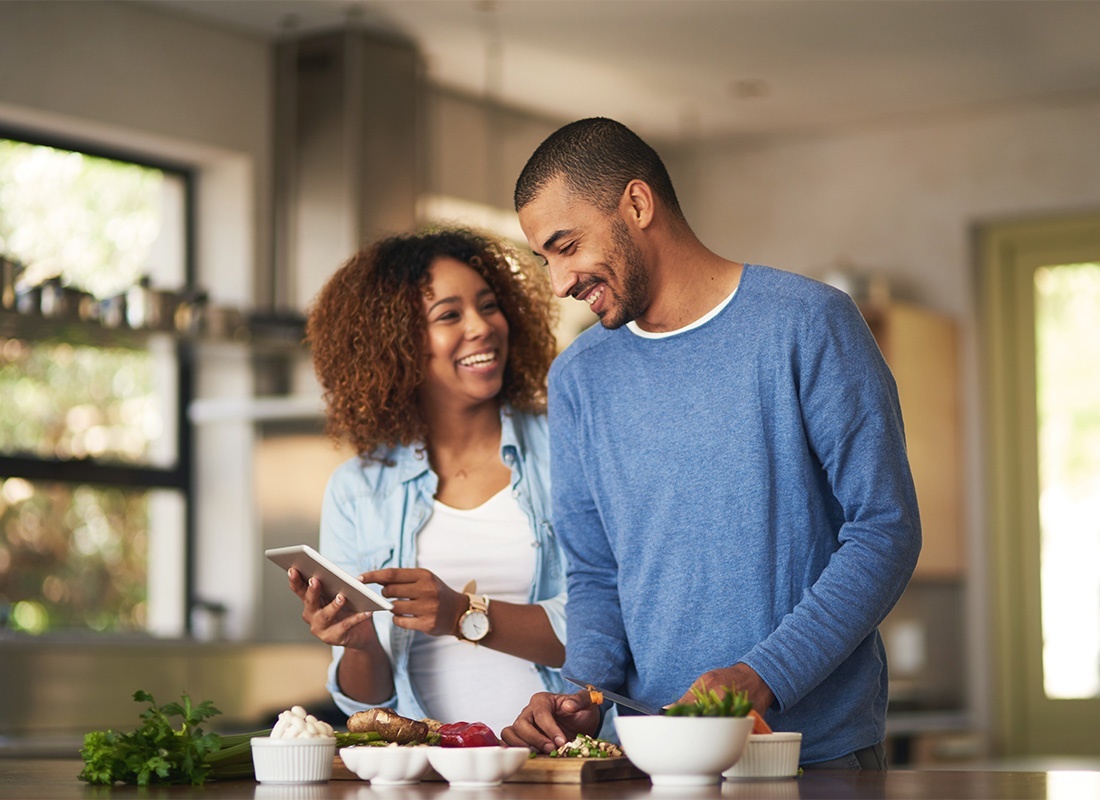 Read Our Reviews - Portrait of a Cheerful Young Married Couple Having Fun Spending Time Together Preparing a Healthy Meal at Home While Using a Phone